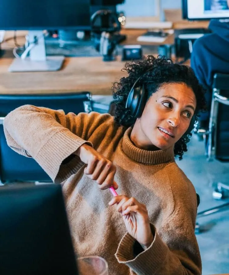 A woman wearing headphones and holding a pen looks across to her colleague