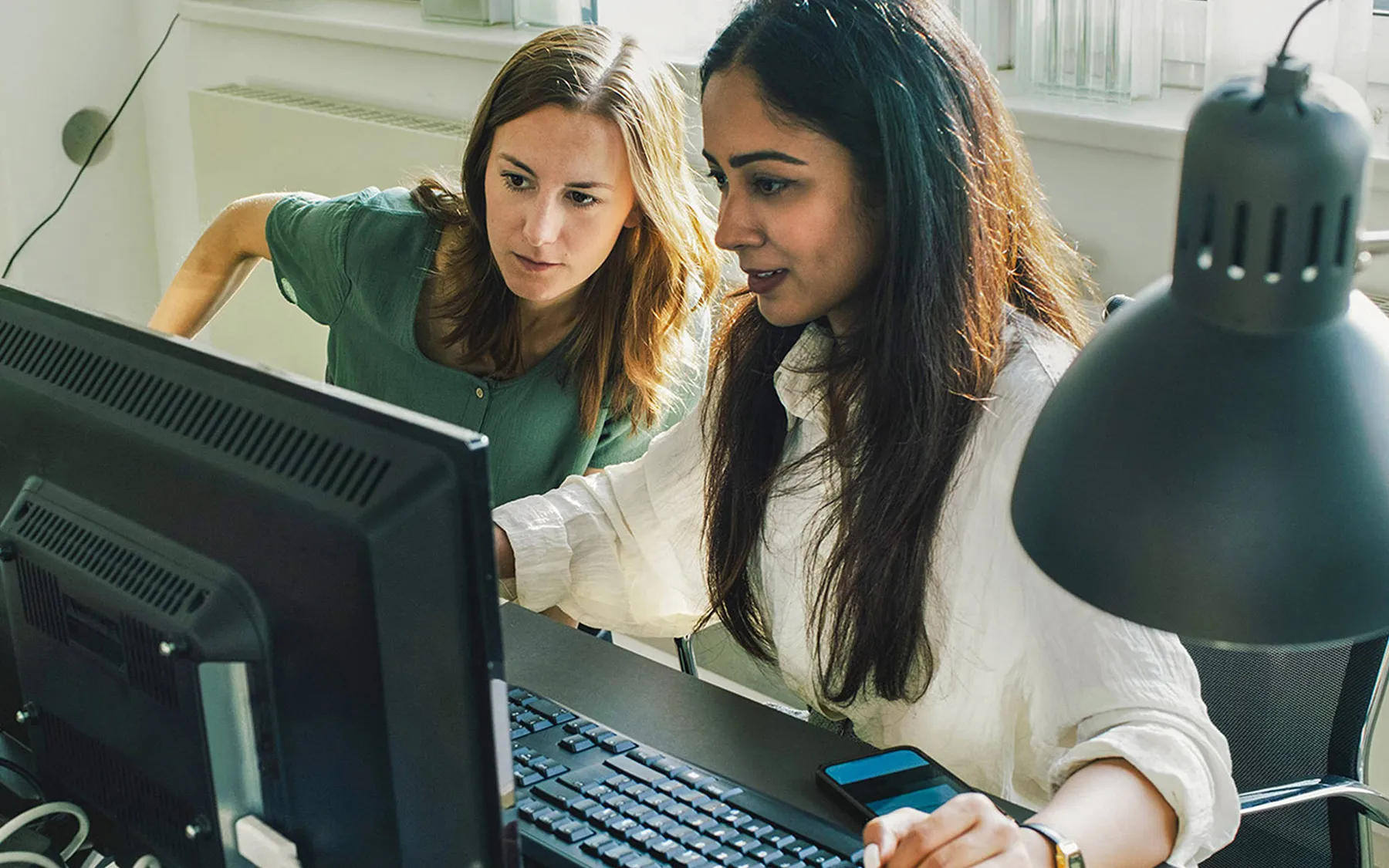 A woman with hands clasped together, working at her desk