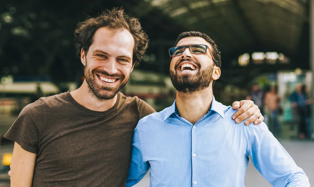 Two men smiling, each with an arm around the other’s shoulders