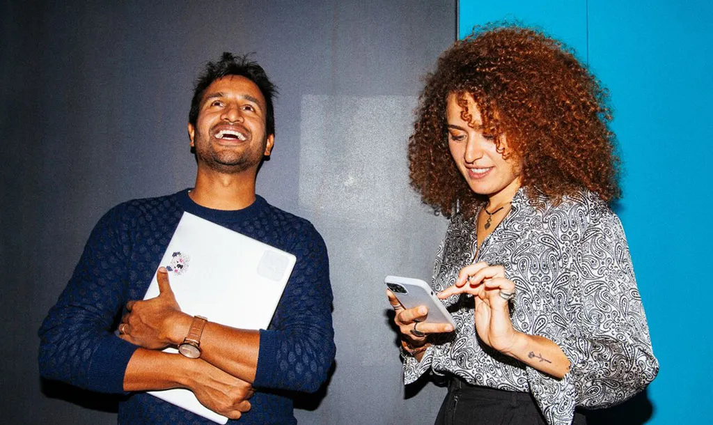 Two people smiling holding a laptop and phone