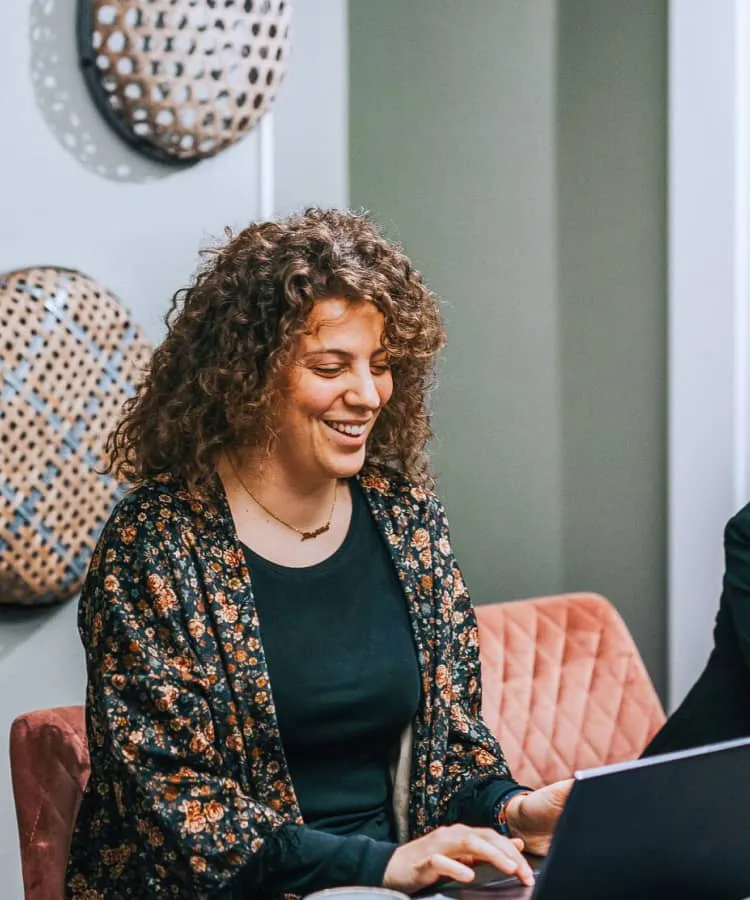 Two women sitting side by side, casually using their laptops
