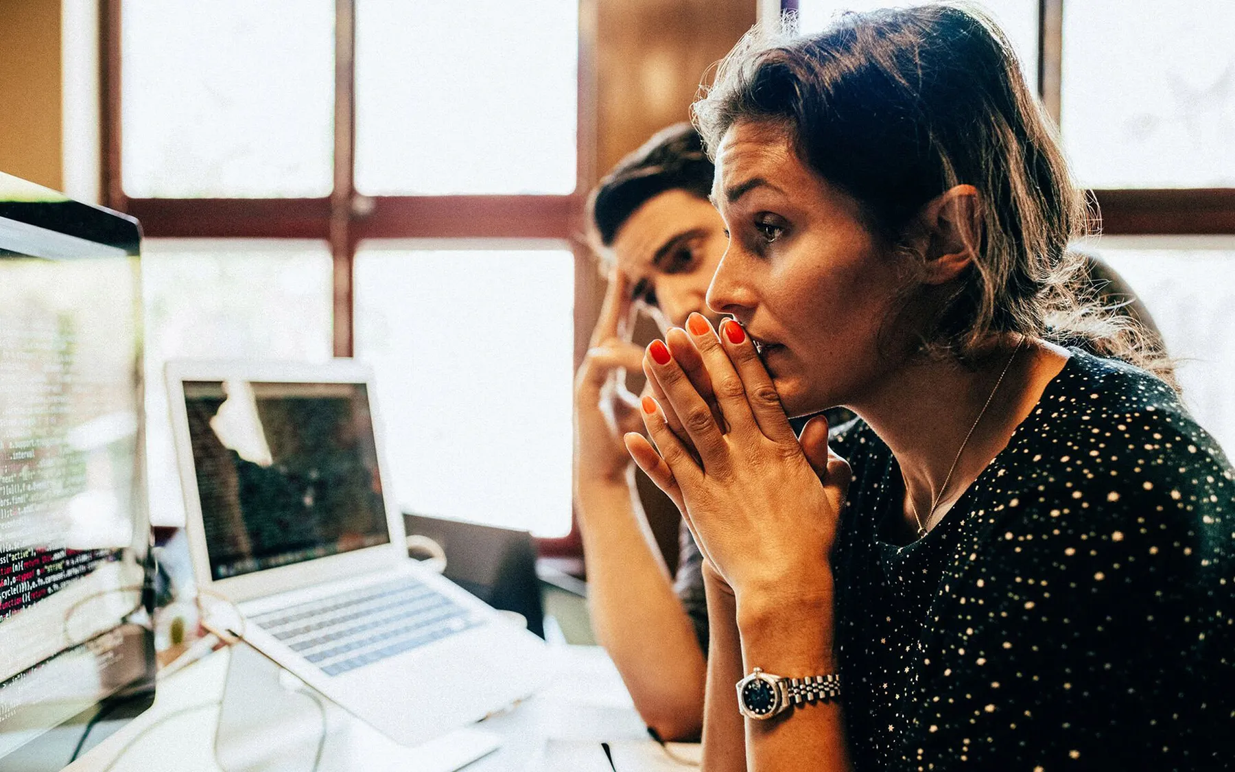 A woman with hands clasped together, working at her desk