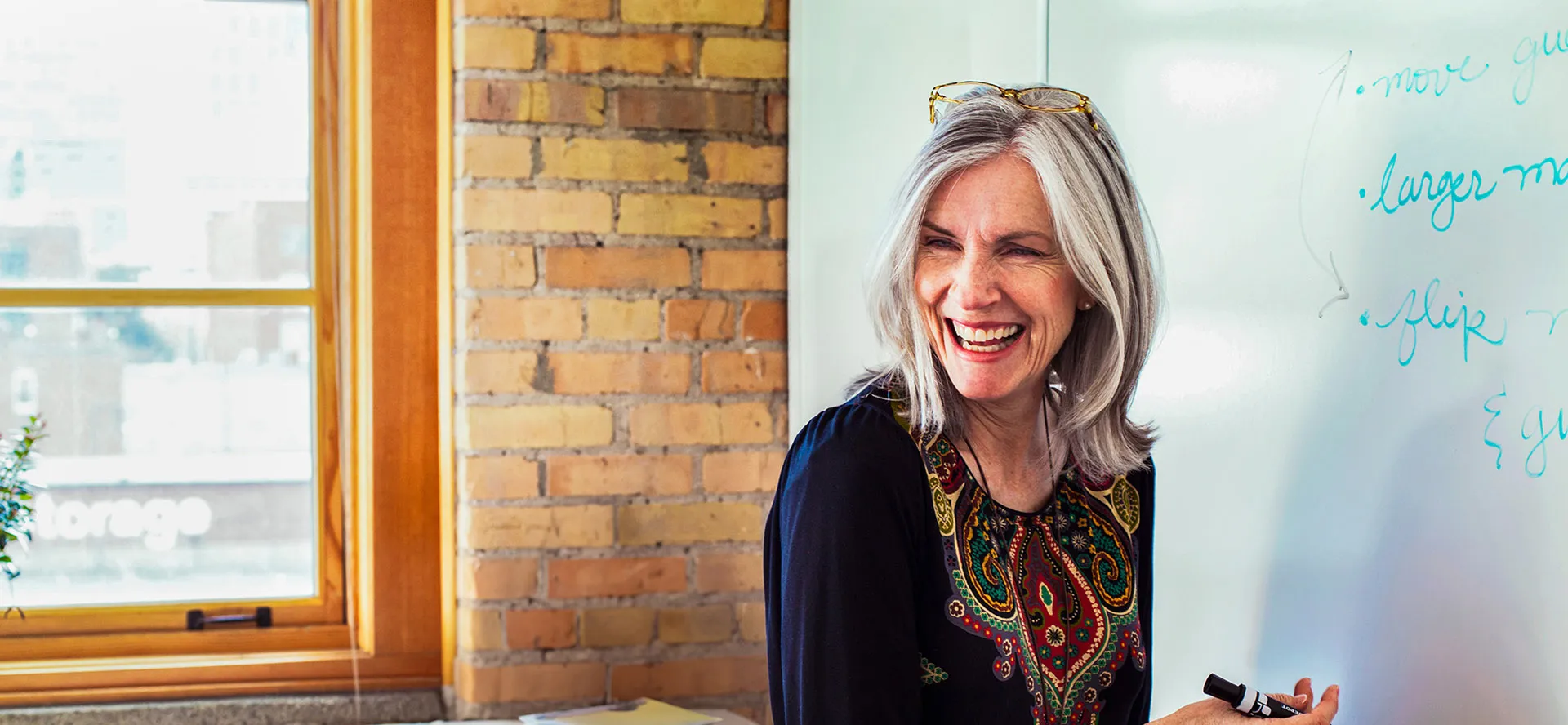 A smiling, grey-haired woman writing on a white board