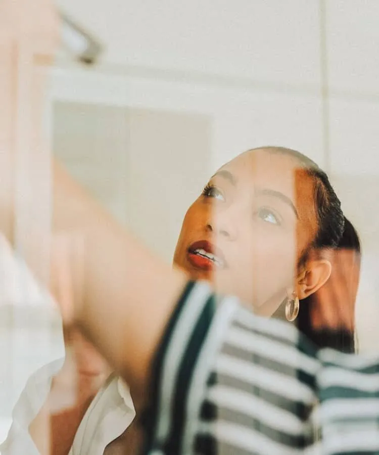 Two young women seen writing on a white board through a glass door