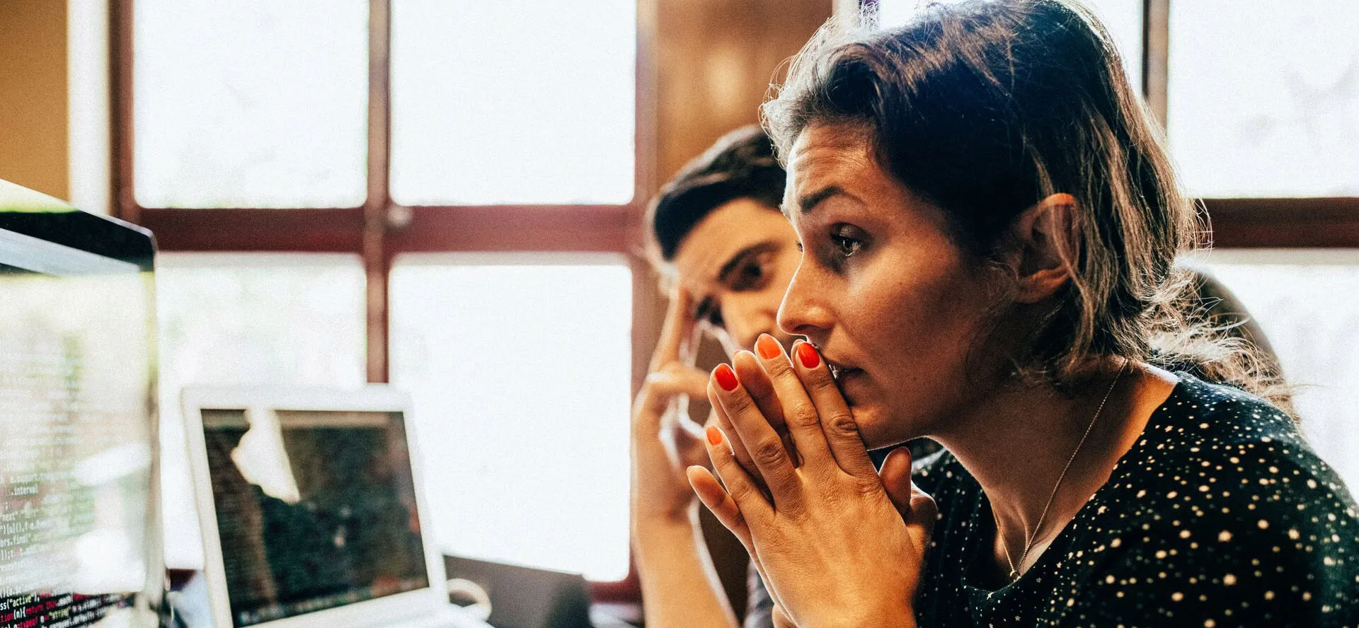 A woman with hands clasped together, working at her desk