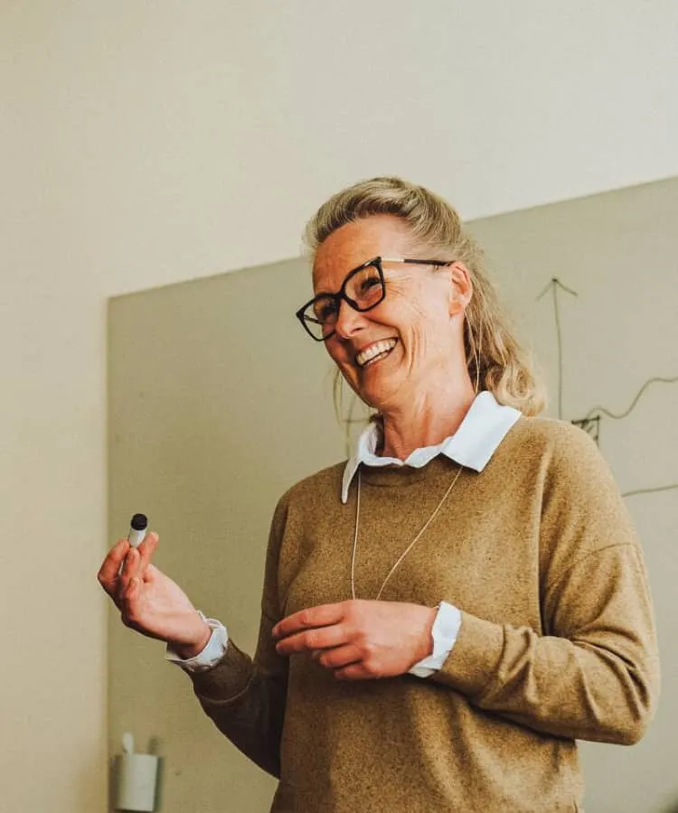 Woman with glasses holding a pen and standing in front of a white board