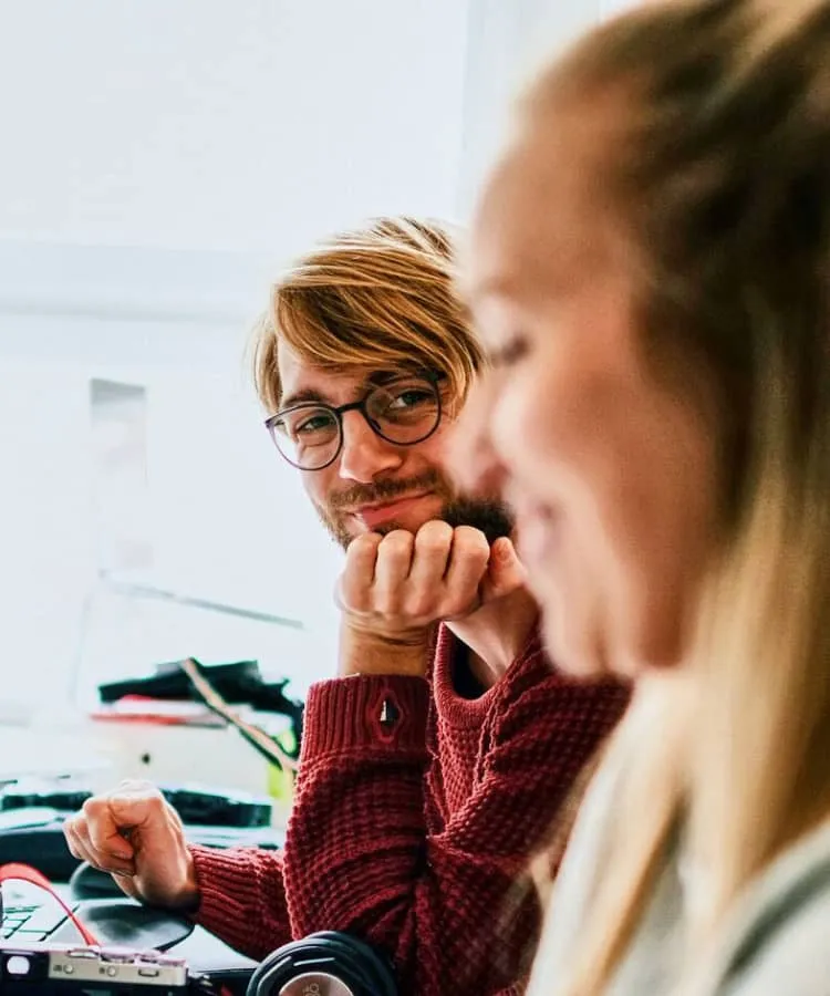 A man with glasses smiling across at a colleague
