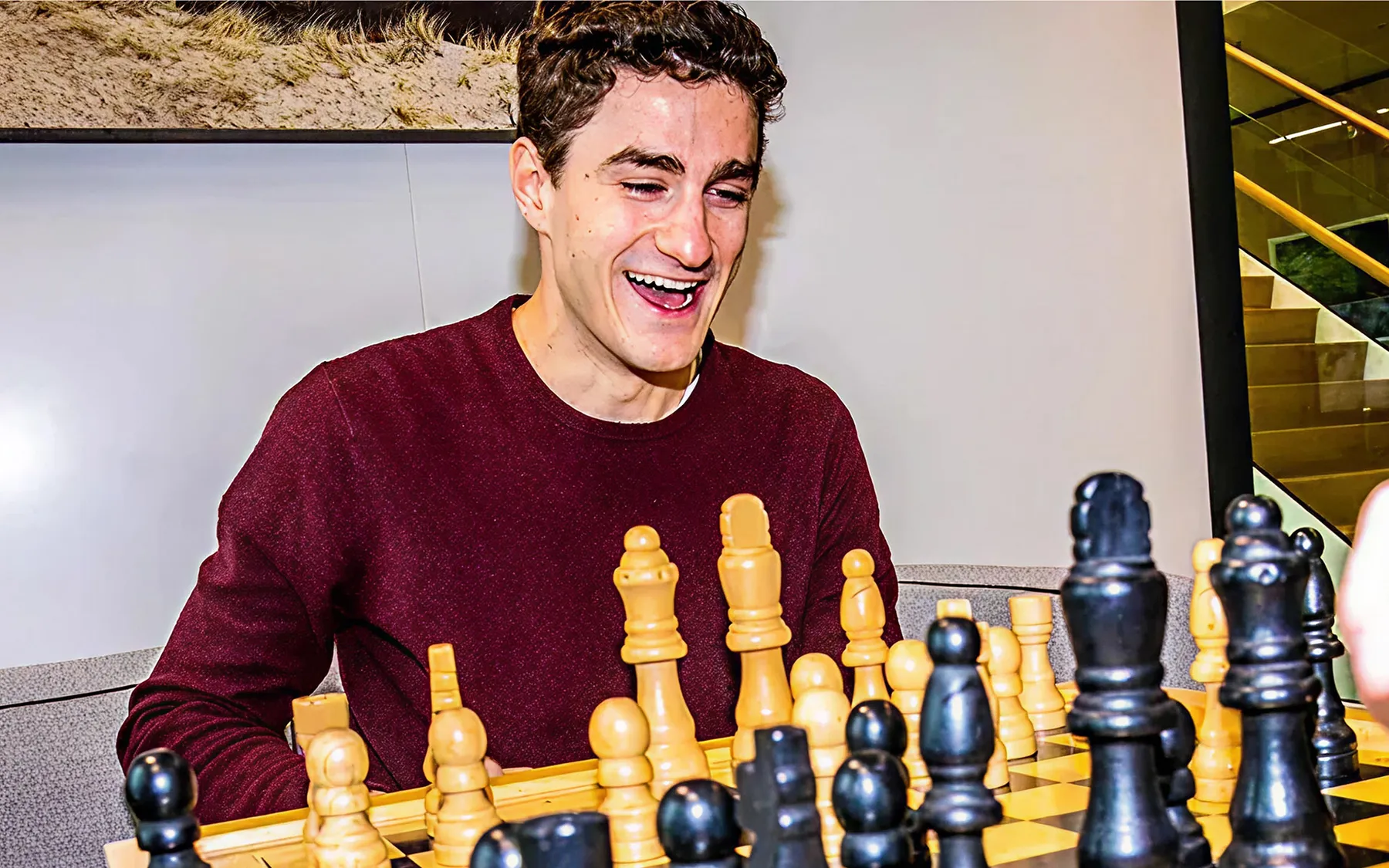 A young man in a burgundy jacket smiling at a chess board