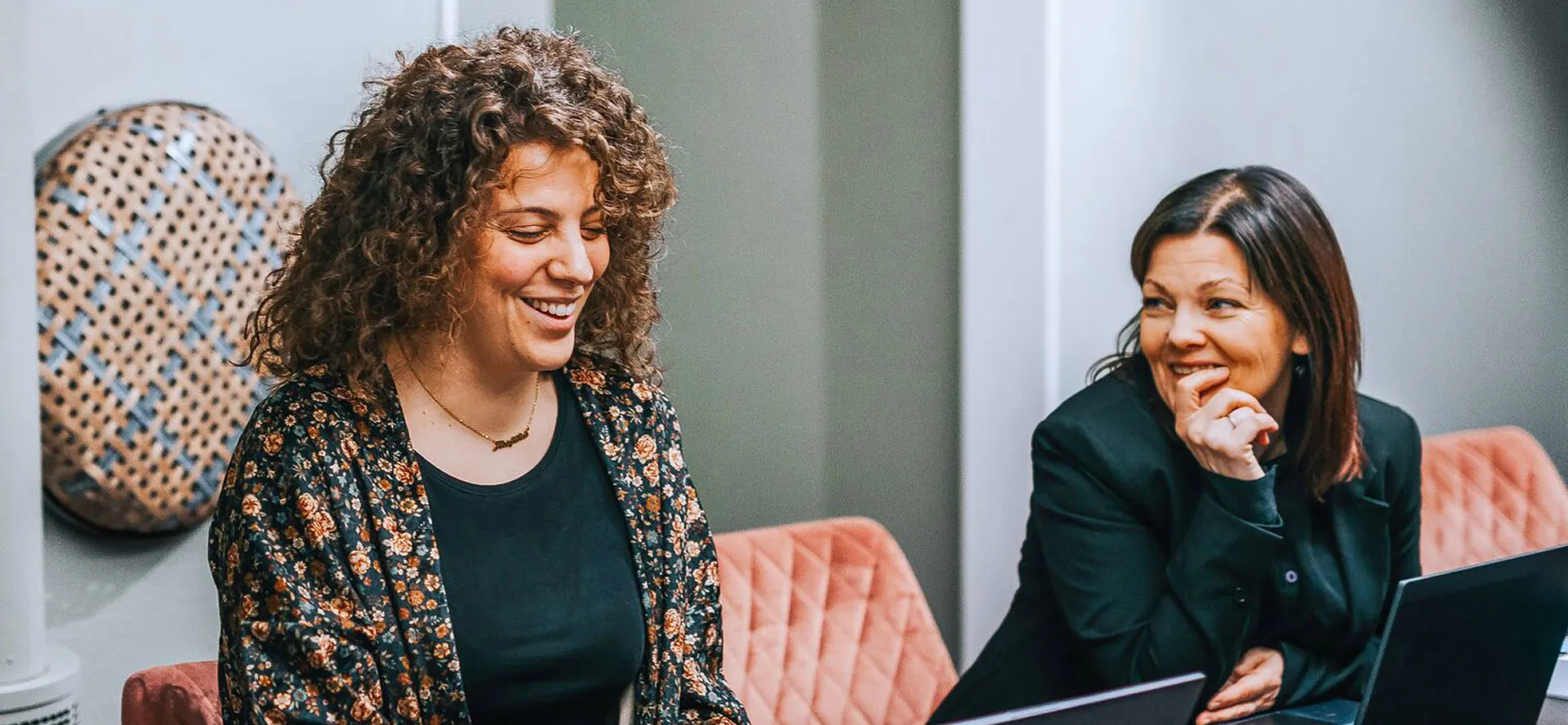Two women sitting side by side, casually using their laptops