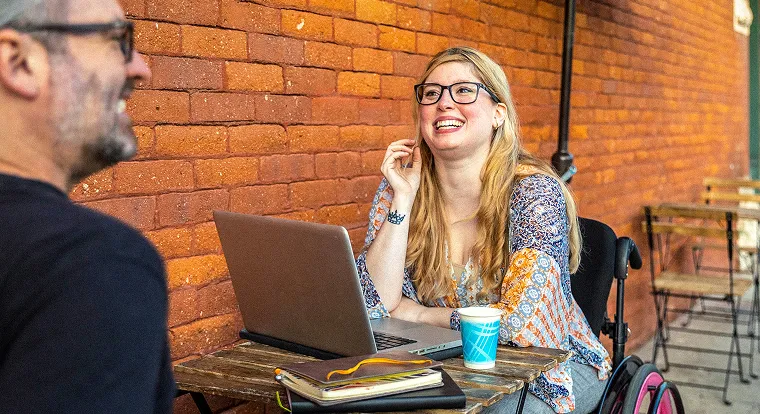 A woman sitting at a table with a laptop looking at a man.