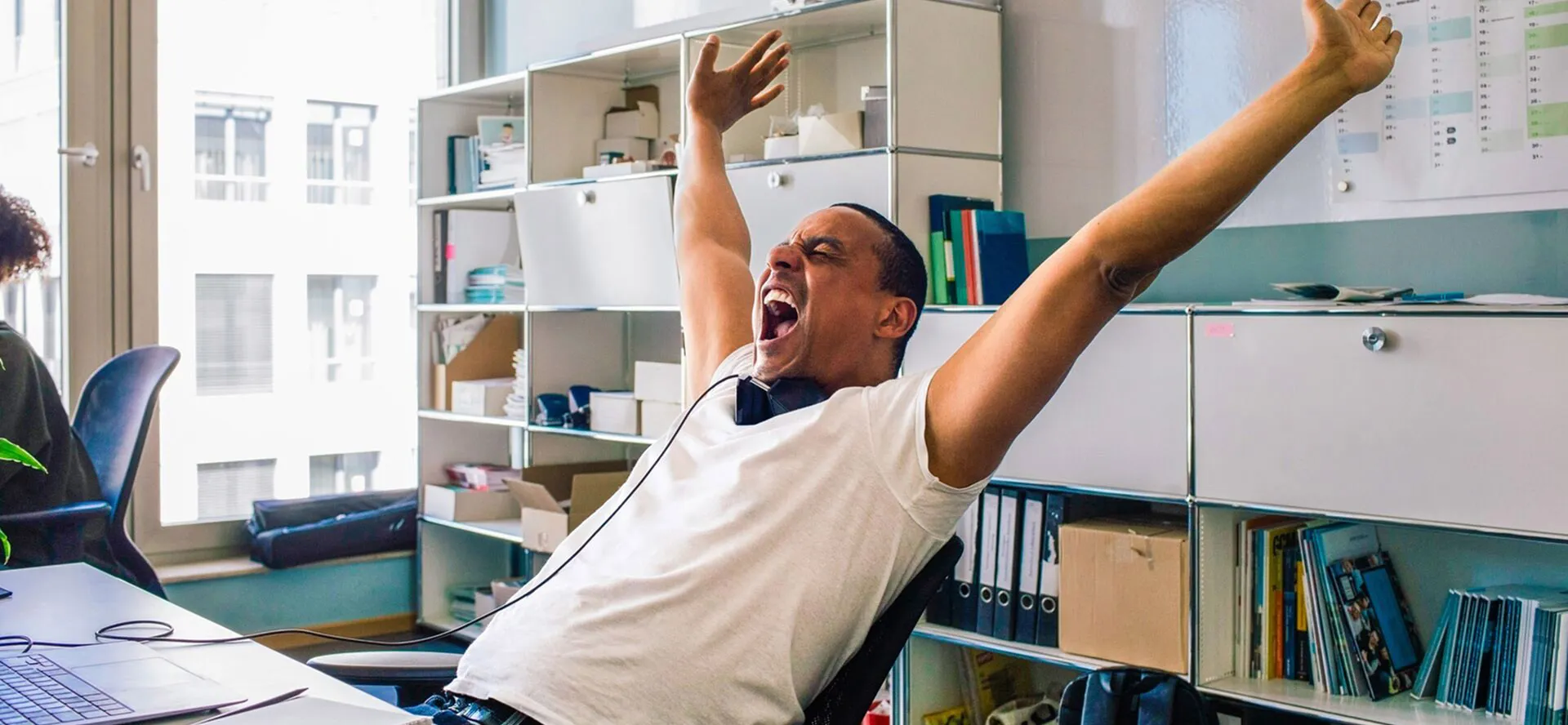 A man leaning back in his chair with arms in the air and mouth open