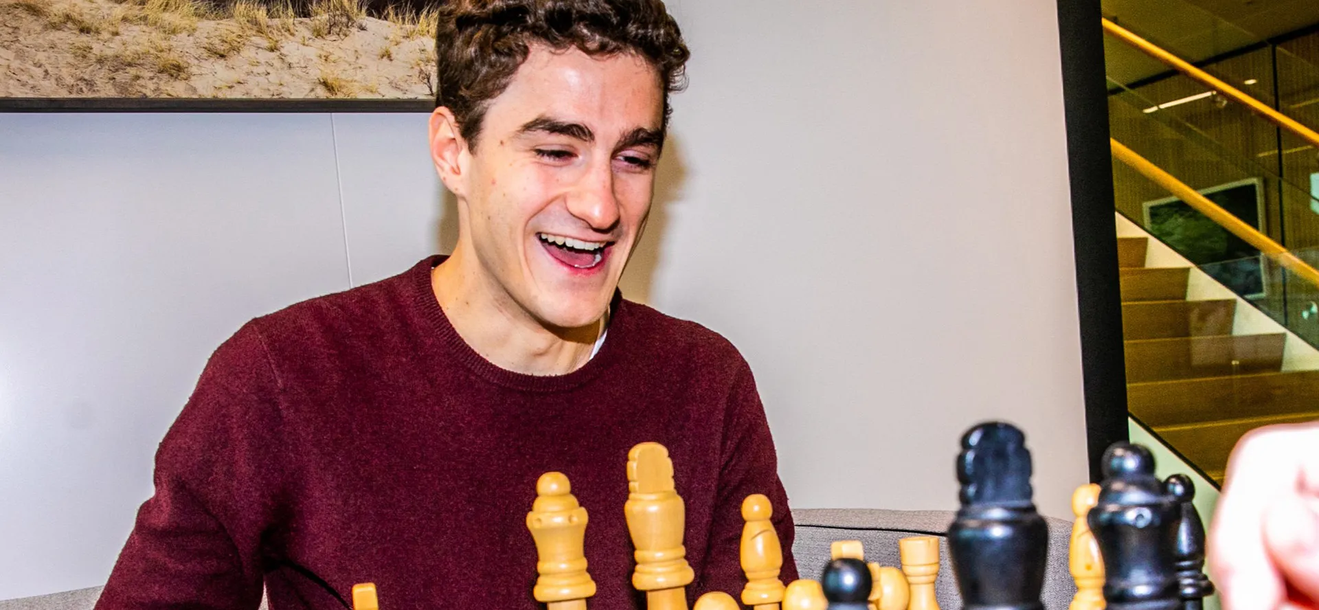 A young man in a burgundy jacket smiling at a chess board