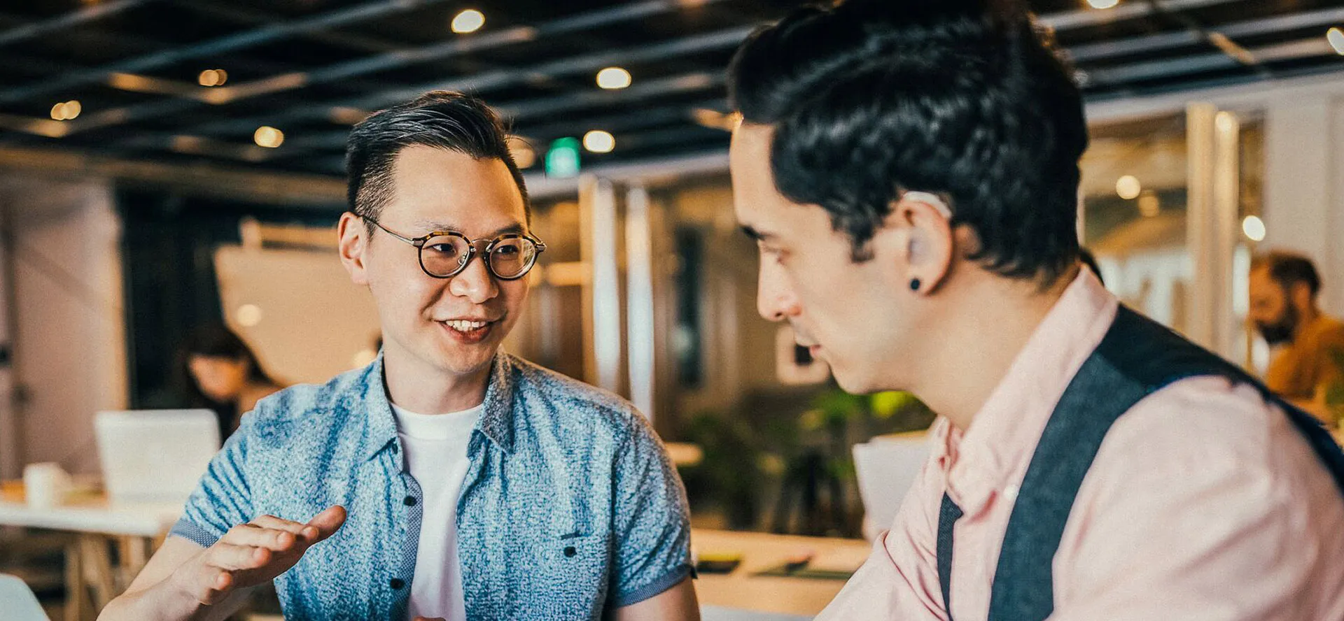 Two men in a breakout space talking and working around a laptop