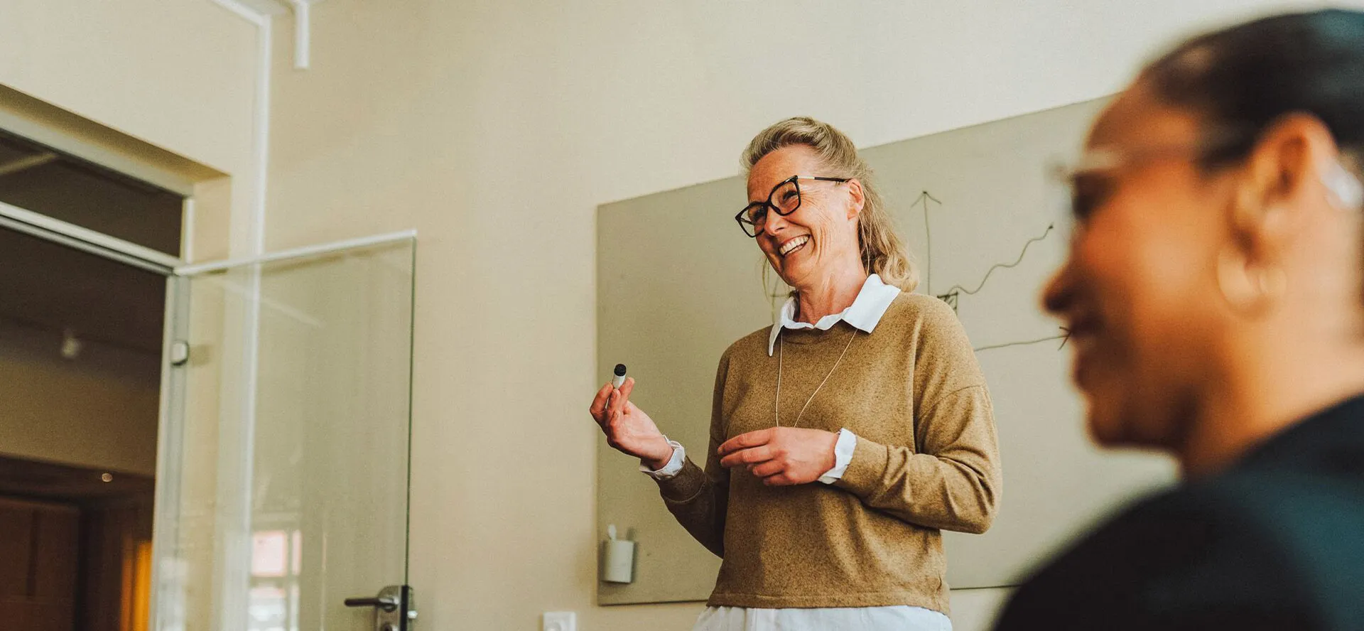 Woman with glasses holding a pen and standing in front of a white board
