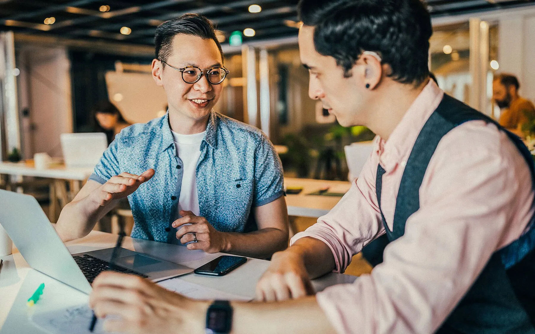 Two men in a breakout space talking and working around a laptop