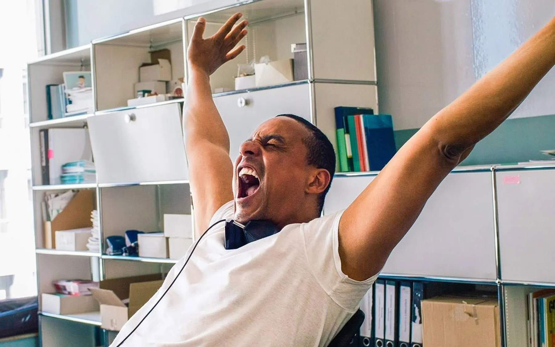 A man leaning back in his chair with arms in the air and mouth open