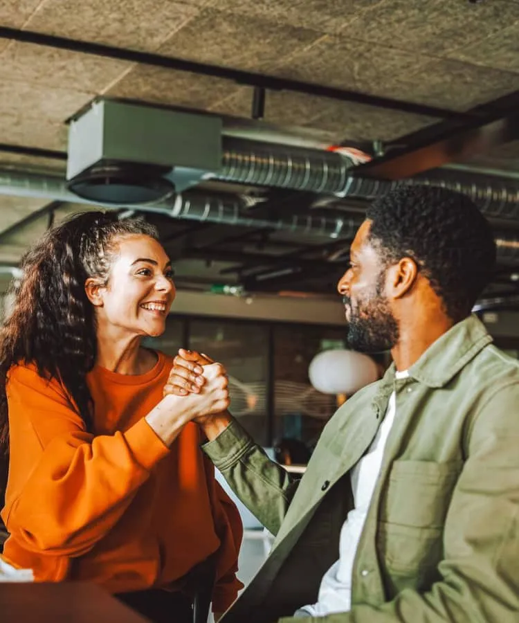 A man and woman shake hands and smile